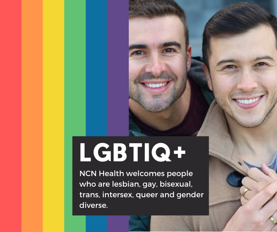 Two young men smiling at the camera, by a LGBTIQ+ rainbow flag.